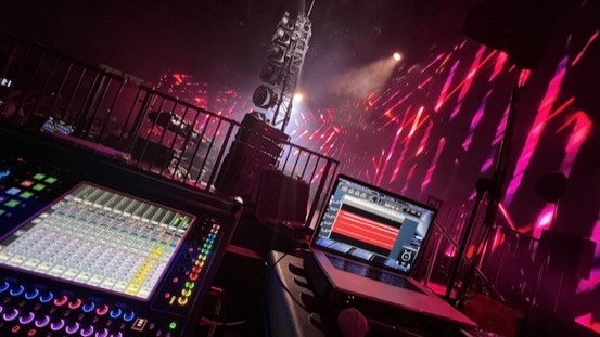 Digital mixing console and a laptop in front of pink stage lighting