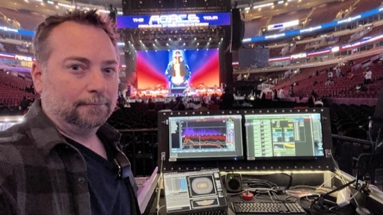 Jeremy Miller at his front-of-house position in an arena, with two measurement screens and the stage behind him