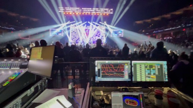 Arena stage with light beams seen from behind the mix position and its screens