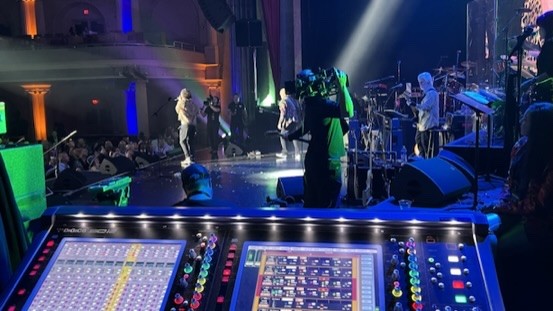 Theater stage with performers and a camera operator, seen from behind the console