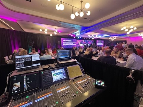 Console and laptops at the audio position in a conference ballroom full of seated attendees