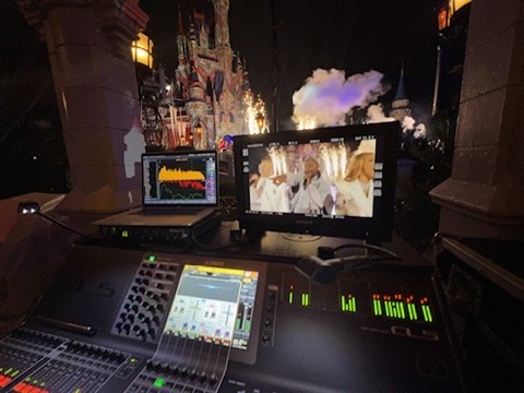 Digital console, laptop and video monitor with a castle and fireworks in the background