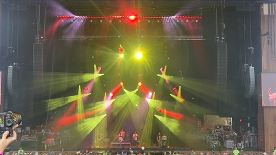 Outdoor amphitheater stage with hung speaker arrays and green and red moving lights