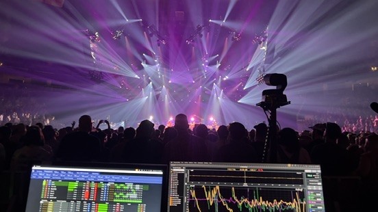 Purple light beams over an arena crowd, with measurement screens in the foreground