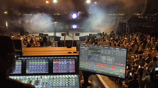 Outdoor night concert with smoke on stage, a console and an analyzer screen in the foreground