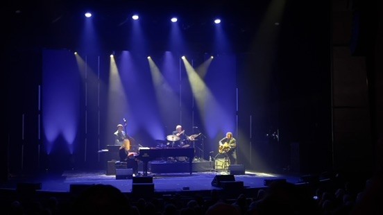 Upright bass, piano and guitar trio on a stage under blue light beams