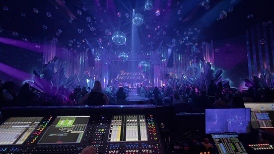 Digital console facing a stage filled with hanging mirror balls and purple light