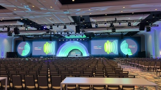 Large hotel ballroom with rows of empty chairs and a curved stage with video screens