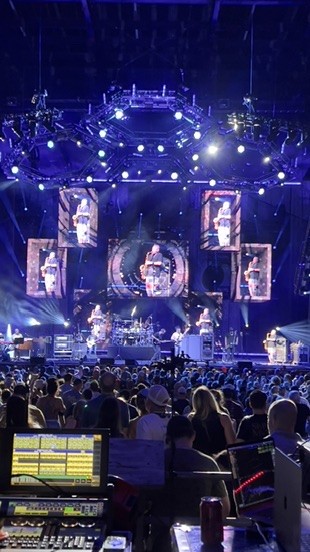 Portrait view of an arena stage with video screens and lighting rigs above the band