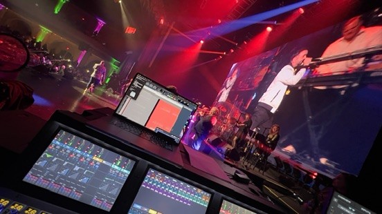 Console touchscreens and a laptop recording session facing a band and a video screen