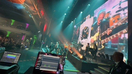 Band on a theater stage with a recording laptop and a mixer screen in the foreground