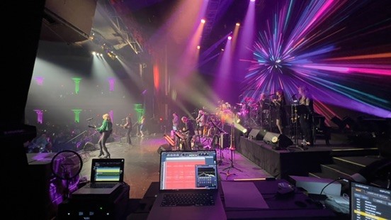 Band on a stage with purple lights and a laptop recording rig at the front