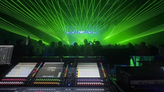 DiGiCo console in the foreground facing a crowd under green laser beams