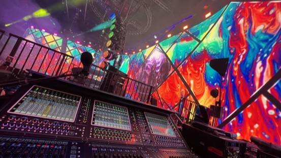 Mixing console on a platform in front of a curved, colorful video wall, shot wide-angle