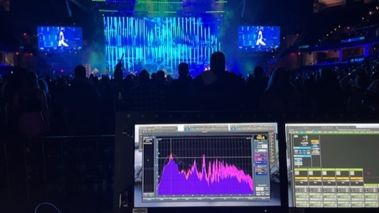 Spectrum analyzer display in the foreground with an arena crowd and a blue video wall behind