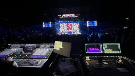 Console and two analyzer screens at front of house facing an arena stage with a large 50 on the video wall